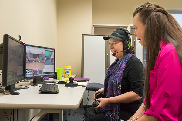 two women looking at dual monitors with headset