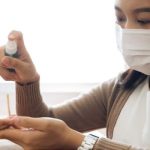 woman with mask using spray bottle on hand