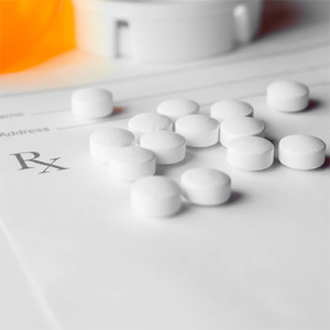 Prescribed pills are scattered on top of a blank RX form, with pill bottles in the background.