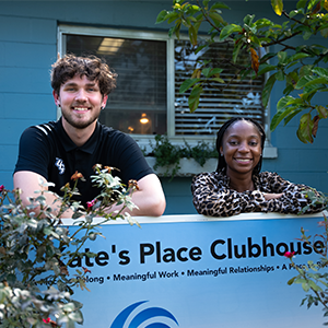 Stephen Conner and Maya Reaves smile in front of the Kate's Place Clubhouse sign