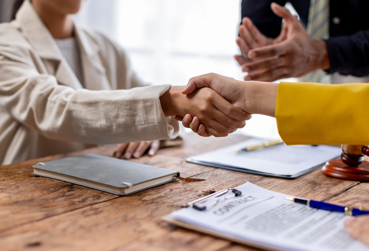 Shaking hands above contracts signed at a table