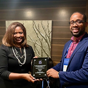 RoSusan Bartee, left, smiles as she accepts an award from a UCEA representative, right. They are standing in front of a wall.