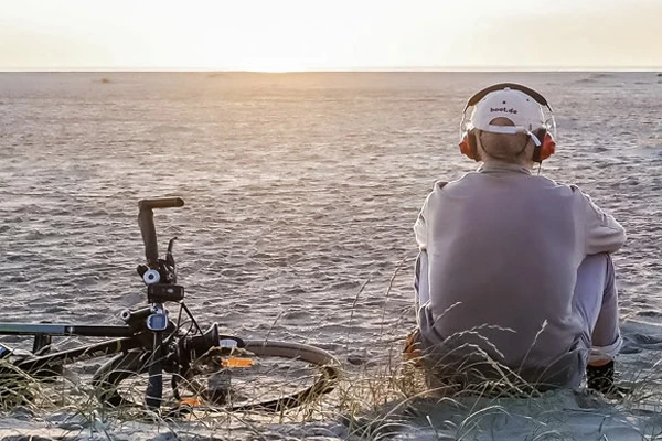 Man sitting on beach with headphones and bicycle