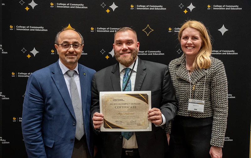 Naim Kapucu, Angel Maldonado and Sarah Bush standing in front of a black CCIE-branded backdrop. Maldonado is holding a Research Impact Showcase presenter certificate.
