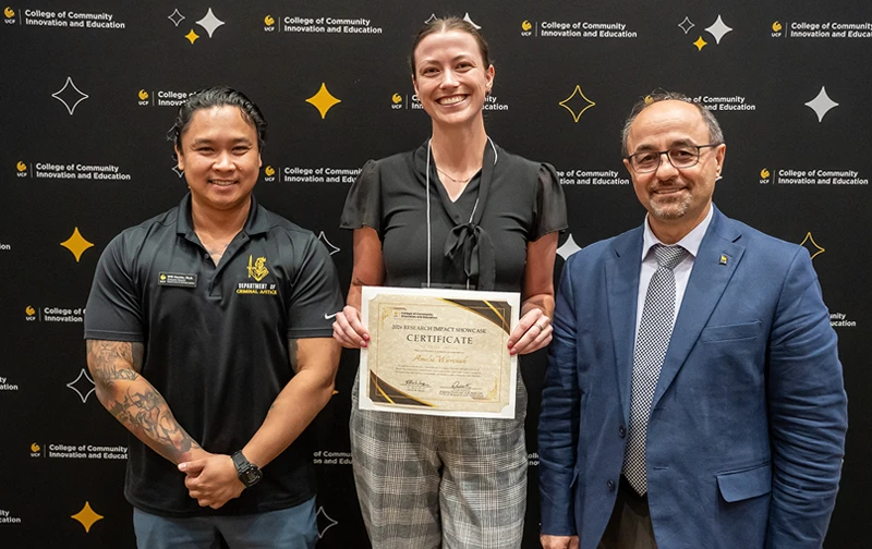 Will Moreto, Amelia Wiercioch and Naim Kapucu standing in front of a black CCIE-branded backdrop. Wiercioch is holding a Research Impact Showcase presenter certificate.