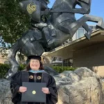 Sarah Hall in cap and gown holding diploma in front of UCF Knight