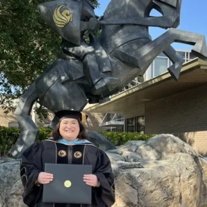 Sarah Hall in cap and gown holding diploma in front of UCF Knight