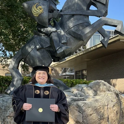 Sarah Hall in cap and gown holding diploma in front of UCF Knight