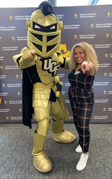 Female student posing with Knightro, pointing fingers at camera