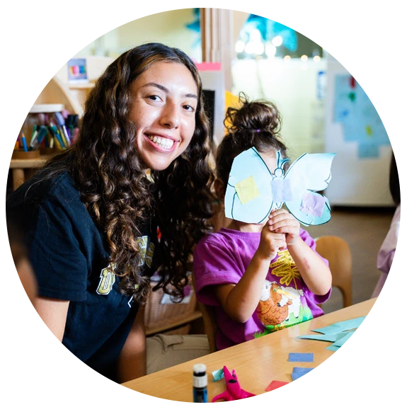 Female student smiling with child holding paper butterfly in front of their face
