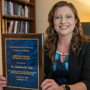 Jacinta Gau sits at her desk, holding her plaque from the American Society of Criminology’s Division of Policing.