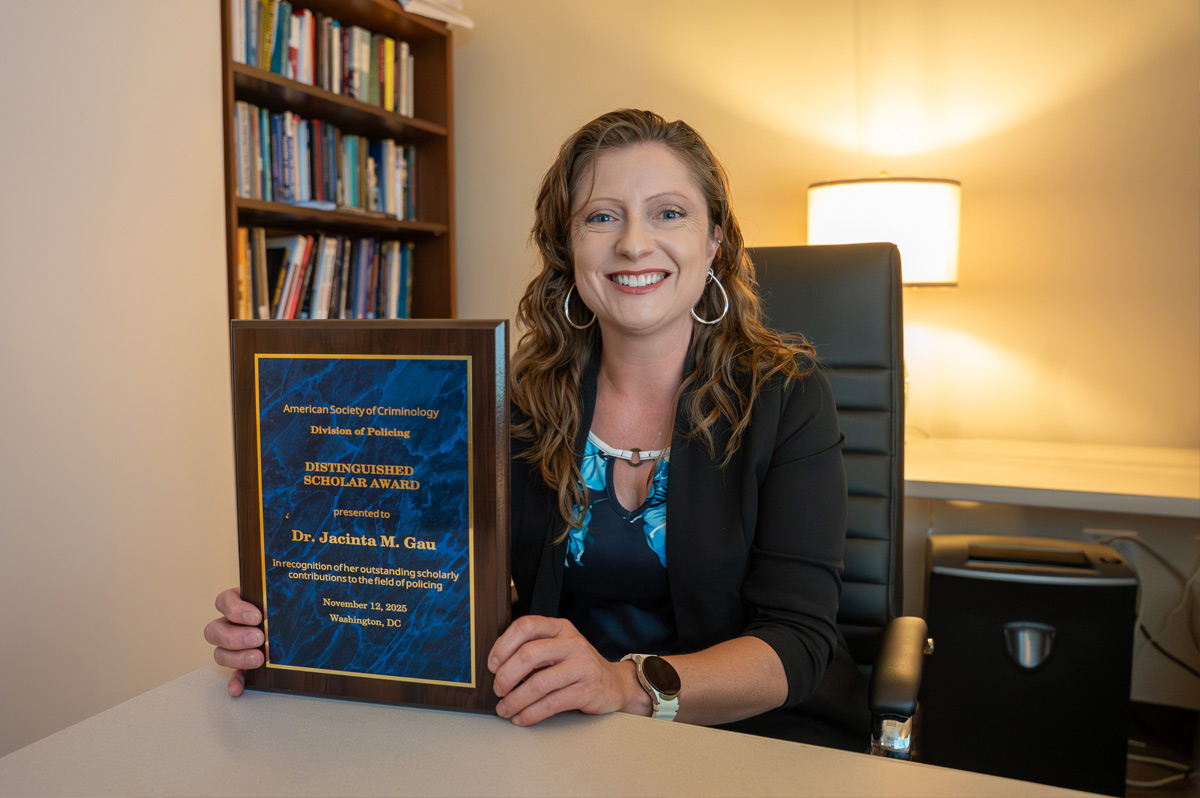 Jacinta Gau sits at her desk, holding her plaque from the American Society of Criminology’s Division of Policing.