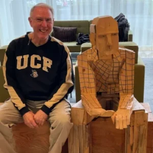 Jim Malcolm sitting and smiling next to statue