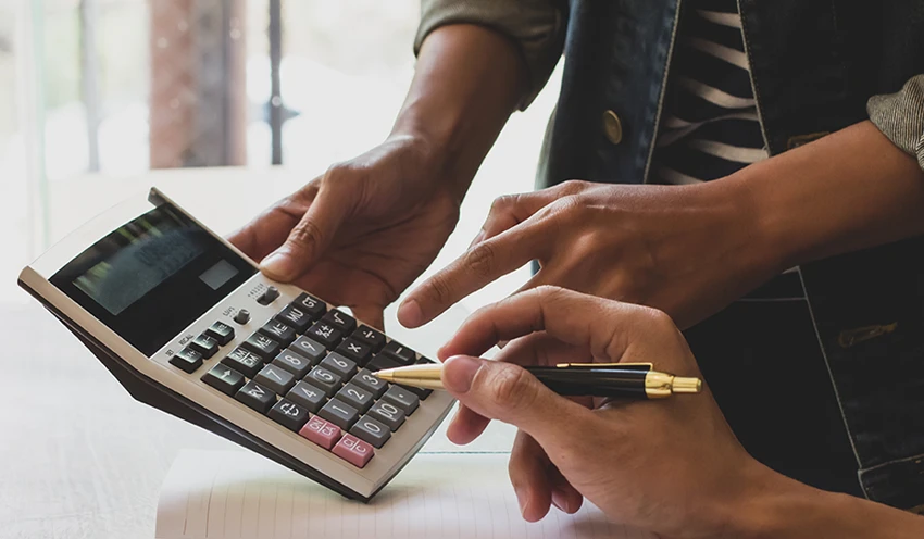 Two sets of hands working with a notebook and calculator